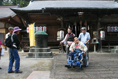大神神社の前に立つ車椅子に乗ったＫさんと他のメンバーの写真