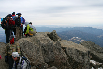 山頂の岩に立つ人たちと霞ヶ浦の写真