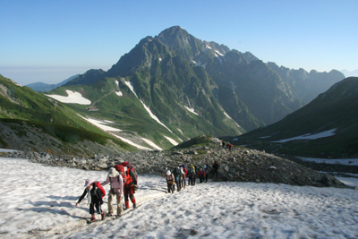 剣岳を背に雪渓を登っている写真