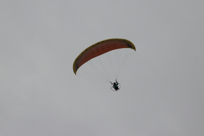 エンジン付きのパラグライダーに乗って空を舞う人の写真