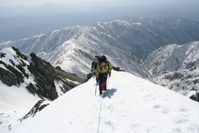 雪壁を登り、山頂への痩せ尾根を登っているメンバーの写真