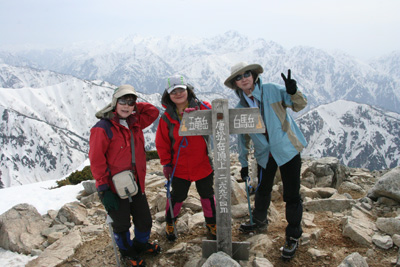 剣岳を背に唐松岳の山頂に立った女性陣の写真