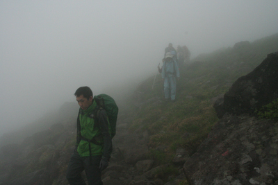 深い霧の中を山頂を背に下っている写真
