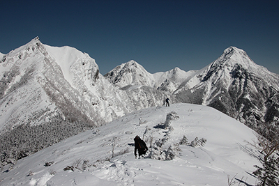 権現岳、阿弥陀岳、中岳、赤岳を背に尾根を下っているKNさんの写真