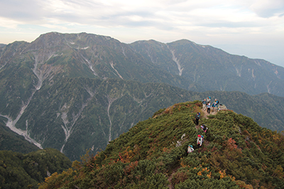 大日連山をバックに標高2,600mのピークを過ぎたところを歩いている写真