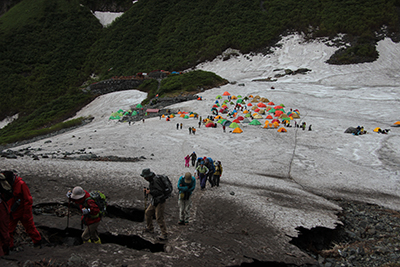 涸沢のテント村を背に雪渓を登っている写真