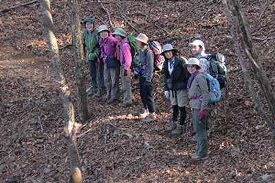 落ち葉の多い登山道に集まった女性陣と黒一点の写真