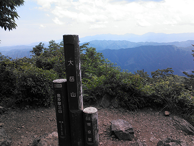 大岳山山頂の標識と背後の山の写真