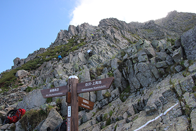 紀美子平の道標と前穂の山頂に登る人たちの写真