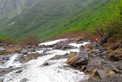 雨の中、涸沢直下の雪渓付近を登っている写真