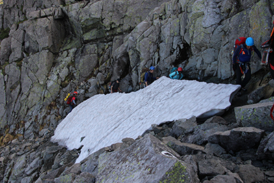 吊り尾根にわずかに残る雪渓の横を歩いている写真