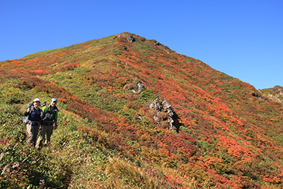 万太郎山の新潟県側山腹のすばらしい紅葉を背にポーズを取る２人の写真