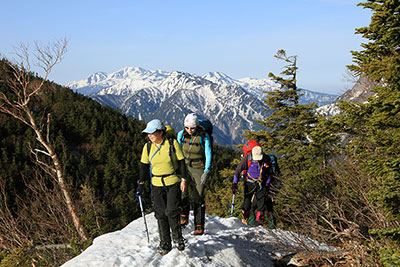 乗鞍岳を背に雪稜を歩いている写真