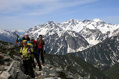 穂高連峰を背に登ってきた４人の写真