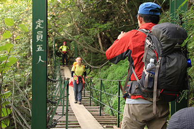 登山道にかかる吊り橋を渡っているＫさんとそれを撮影しているＣさんの写真