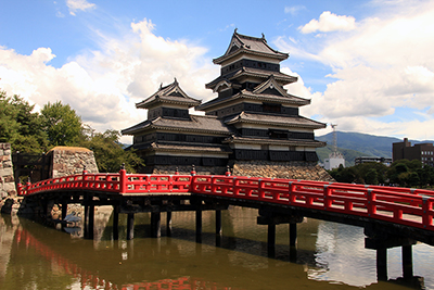 お堀にかかる赤い橋と松本城の写真