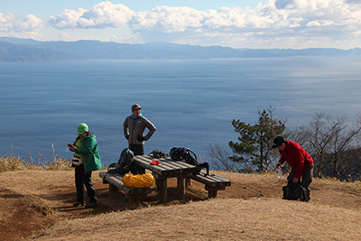 海と伊豆半島が見える山頂でくつろぐメンバーの写真