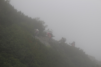 深い霧の中で八本歯のコル手前を登ってくるメンバーの写真