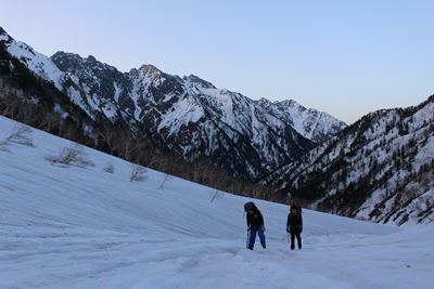 穂高連峰を背に日の出前の残雪斜面を登っている写真