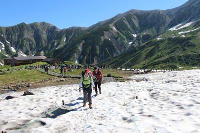 大人数が一ノ越に向かう登山道から別れて室堂山に向けて雪渓を歩いている写真
