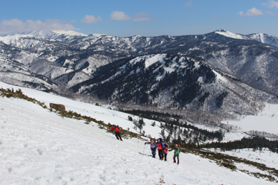 平ガ岳や景鶴山を背にして雪の斜面を登っている写真