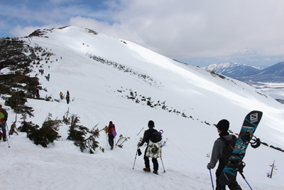 至仏山を背に下るメンバーとスノボー等を背負って登る人たちの写真