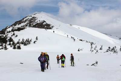 小至仏山を背に雪原を歩き、鳩待峠に向かっているメンバーの写真