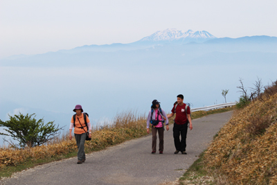 御嶽山を背に車道を歩いているメンバーの写真