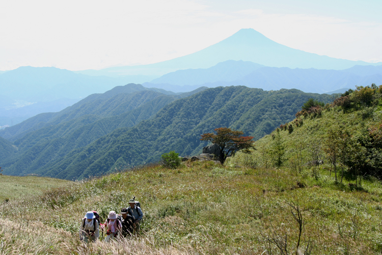 富士を背に黒岳の草原を歩く人の写真