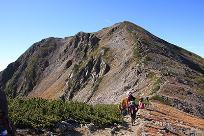 赤石岳山頂を背に稜線を歩いている写真