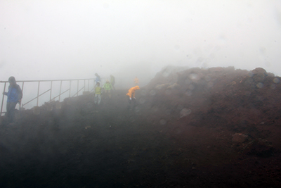 寒い霧雨の中、剣ヶ峰直下の滑りやすい斜面を下っている写真