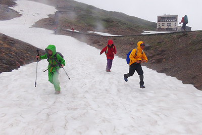 登山道横の雪渓を走る子どもたちの写真