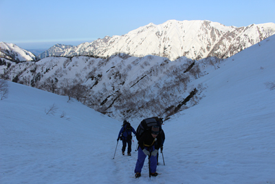 抜戸岳や笠ヶ岳を背に稜線まで続く残雪の斜面をがんばって登っている写真