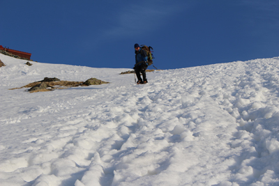 雪の急斜面を青空を背に下っているTさんの写真